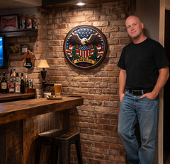 Man standing in a bar with a decorative wall emblem and bar setup.