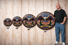 Man standing next to decorative wall plates with eagle design and size measurements on a wooden panel background.